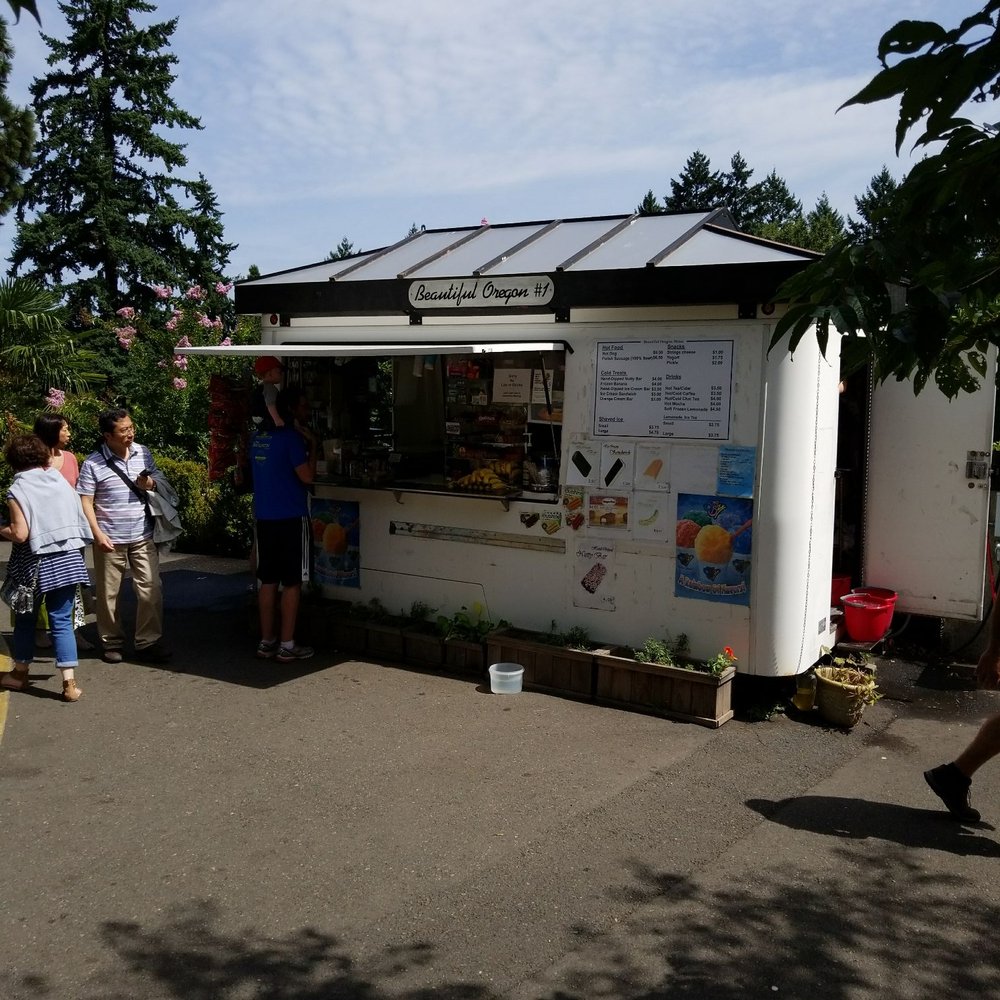 a group of people standing in front of a food stand a group of people standing in front of a food stand