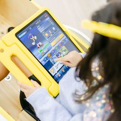 A child with sparkling sleeves plays a Sonic game on a tablet in a bright yellow case.