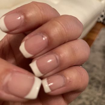 Star Nails & Spa - Gel manicure - A hand with neatly manicured French nails is shown, with a blurred background of a room interior. - Nail Salons Near Me - Hingham, Massachusetts