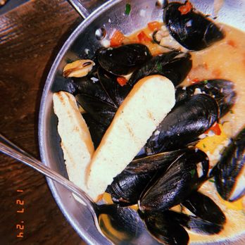 Sulmona - Mussels Antipasti - Mussels are served in a metal bowl with a creamy sauce, garnished with chopped vegetables and two slices of bread. - Pizza Near Me - Cambridge, Massachusetts