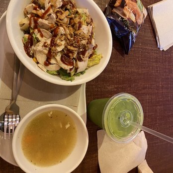 Panera Bread - A meal consisting of a salad with chicken and dressing, a bowl of clear soup, and a green beverage in a plastic cup with a straw is on a wooden table. - Sandwiches Near Me - Tinley Park, Illinois