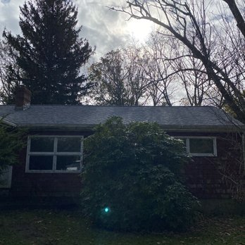 Vaz Construction - After - A residential house with a large bush in front, set against a backdrop of tall trees and a cloudy sky, with sunlight peeking through. - Roofing Near Me - New Bedford, Massachusetts