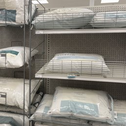 Pillows - Multiple pillows are arranged on metal shelves in a retail store, with packaging labels visible.