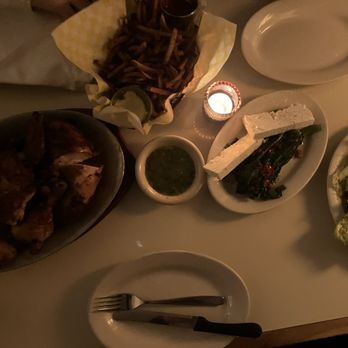 The Fly - Full Chicken // Fries // Broccolini with Feta // Caesar Salad - A dinner table with a variety of Mexican dishes, including a bowl of grilled chicken, a basket of French fries, a small bowl of green salsa, grilled vegetables with cheese, and a salad. The table is dimly lit with a small candle, and there are plates, utensils, and a napkin visible. - Wine Bars Near Me - Brooklyn, New York