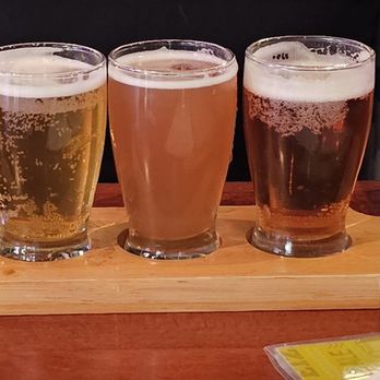 Union Draft House - Flight - Four glasses of different beers are arranged on a wooden flight paddle at a bar, showcasing a variety of beer styles. - Sports Bars Near Me - El Paso, Texas