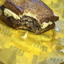 A cheeseburger with melted cheese and cooked beef patty on toasted bread, partially eaten, on yellow branded paper.