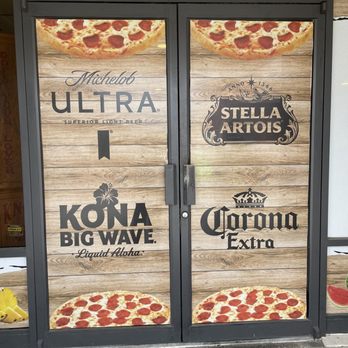 Apollo Pizza - the front door of a restaurant - The image shows a storefront with two glass doors framed in black, displaying pizza images at the top and bottom. The doors have logos of beer brands including Ultra, Stella Artois, Kona Big Wave, and Corona Extra, on a wood-textured background. The sign above reads 'APOLLO PIZZA'. - Pizza Near Me - Apollo Beach, Florida
