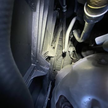 Firestone Complete Auto Care - Oil pooled at the bottom of engine bay, likely spilled while filling and not cleaned up. What would I know though, right? - Oil pooled at the bottom of the engine bay, indicating a spill during oil filling, with visible engine components and pipes. - Tires Near Me - Plainfield, Illinois
