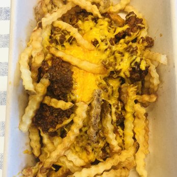 Mighty Fine Burgers Cedar Park - Chili Cheese Fries - Crinkle-cut fries are topped with chili and melted cheese, served in a rectangular white container. The fries are golden and crispy, with some chili and cheese visible on top. - Burgers Near Me - Cedar Park, Texas