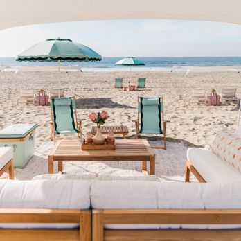 The Barbara Beach Club - Cushioned lounge seating under a canopy on a sandy beach, with turquoise umbrellas and ocean views. - Beach Equipment Rentals Near Me The Barbara Beach Club - Cushioned lounge seating under a canopy on a sandy beach, with turquoise umbrellas and ocean views. - Beach Equipment Rentals Near Me