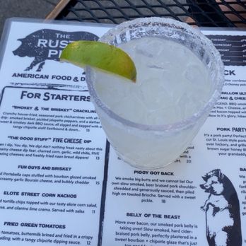The Rusty Pig - Margarita - A clear cocktail with ice and a lime wedge is placed on a menu at The Rusty Pig restaurant in Geneva, NY, featuring smoked meats and barbecue. - Barbeque Near Me - Geneva, New York