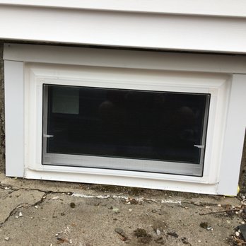 Rite Window of Massachusetts - A rectangular basement window with a white frame is set into a stone foundation wall, with a concrete sidewalk in front. - Windows Installation Near Me - Woburn, Massachusetts