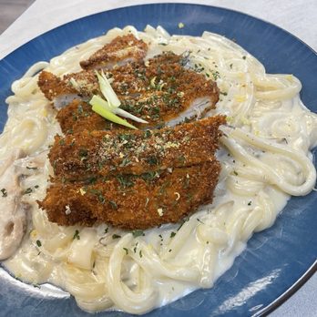 Azure - Creamy udon with shiitake mushrooms. Very yummy - A dish featuring fettuccine pasta coated in a white creamy sauce, topped with breaded and fried chicken cutlets. The chicken is garnished with chopped herbs and grated cheese, and a small piece of green onion is placed on top. The dish is served on a blue plate, placed on a light-colored table surface. - Desserts Near Me - Austin, Texas