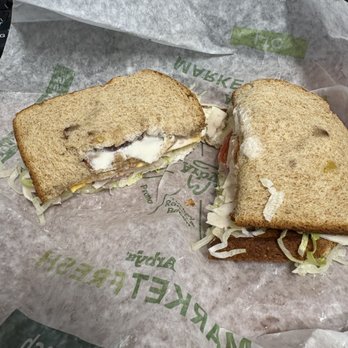 Arby's - A sandwich with visible lettuce, tomato, and mayonnaise is cut in half, showing the filling inside. The bread is toasted and the sandwich is placed on branded paper from Subway, with some shredded lettuce around. The sandwich appears to be a typical Subway sub with fresh ingredients. - Fast Food Near Me - Temecula, California