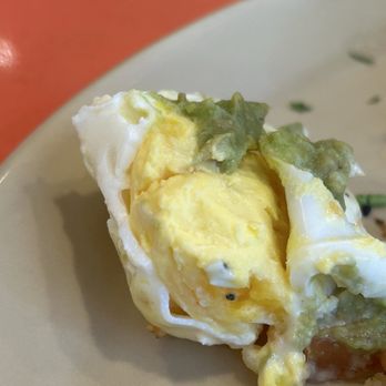 Snooze, an A.M. Eatery - Over cooked "poached" egg - A partially eaten cooked egg with a yellow yolk and white, topped with greenish sauce or garnish, on a beige plate. - Breakfast & Brunch Near Me - Gilbert, Arizona
