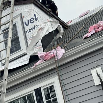 Storm King Roofing - Two workers are on the roof of a house, working near the chimney, with construction materials and tools visible. - Roofing Near Me