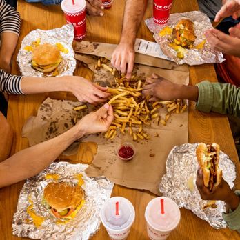 Five Guys - A top-down photograph of a group of friends sharing an order of fries alongside their sandwiches at a Five Guys restaurant. - Burgers Near Me - Pinecrest, Florida Five Guys - A top-down photograph of a group of friends sharing an order of fries alongside their sandwiches at a Five Guys restaurant. - Burgers Near Me - Pinecrest, Florida