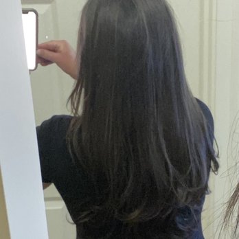 HC Studio - Love the V shape and gentle curls she gave me - A woman with long, dark, wavy hair is standing in front of a mirror, capturing a photo with her phone. She is wearing a black top and is positioned with her back to the camera, with her hair falling past her shoulders. The background features a white door with a paneled design. - Hair Salons Near Me - Brookline, Massachusetts