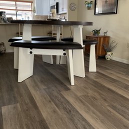 Beautiful laminate flooring. - A home dining space features a dark wood table with black cushioned benches, a wooden sideboard, and wall decorations, with a kitchen visible in the background.