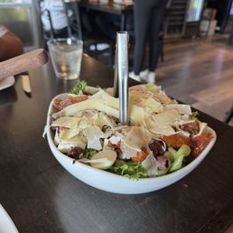 Build Your Own Salad - A large salad bowl with cheese shavings and vegetables, placed on a dark wooden table in a restaurant setting.