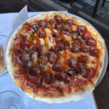 Antico Posto - Hot Honey Pepperoni - A pizza with a thin, slightly crispy crust topped with melted cheese, tomato sauce, and numerous pepperoni slices. The pizza is placed on a round tray on a table, with a glass of water nearby and a restaurant setting in the background. - Italian Near Me - Oak Brook, Illinois