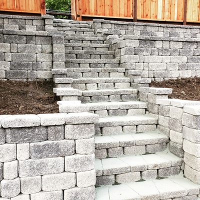 Stone Retaining Wall - Stone retaining wall using Calstone Product. Multi tiered wall as the hillside slope was significant to create only one wall. Steps going down are the same product as the wall blocks, with a top cap piece to give the wall a completed finished look. Stone Retaining Wall - Stone retaining wall using Calstone Product. Multi tiered wall as the hillside slope was significant to create only one wall. Steps going down are the same product as the wall blocks, with a top cap piece to give the wall a completed finished look.