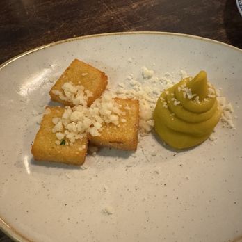 Thistle & Leek - Crispy polenta fritters - Three golden, crispy polenta fritters are served on a white plate, garnished with crumbled cheese and accompanied by a swirl of green sauce. - Gastropubs Near Me - Newton, Massachusetts