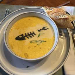 Soup - A bowl of creamy soup with a fishbone design made from dark sauce, accompanied by a piece of bread on a plate.