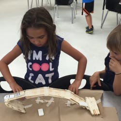 Two campers test the durability of their bridge by slowing adding dominoes to represent cars.