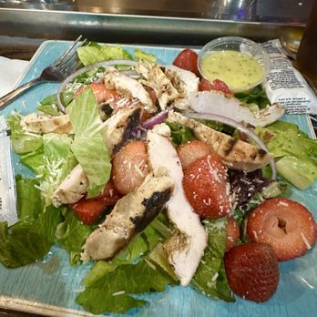 D'arcy's Pint - Strawberry Salad - A salad featuring grilled chicken strips, fresh strawberries, lettuce, and shredded cheese, served with a small cup of dressing on a blue plate. - Irish Near Me - Springfield, Illinois