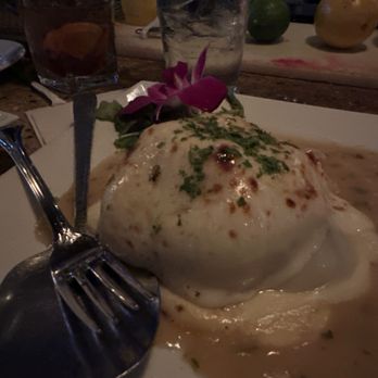 Pace's Steakhouse - Stuffed portobello - A baked dish with melted cheese and herbs is served on a white plate, garnished with a purple flower, with drinks and fruits visible in the background. - Steakhouses Near Me - Hauppauge, New York