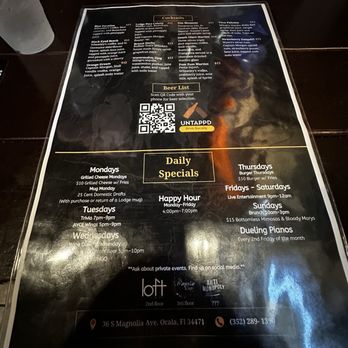 The Lodge - Menu - July 2025 - A menu printed on paper is placed on a dark wooden table at The Lodge in Ocala, FL. The menu includes sections for cocktails, a QR code for beer selection, daily specials such as happy hour, and entertainment events. The menu also provides the address and contact information for the venue. - Gastropubs Near Me - Ocala, Florida
