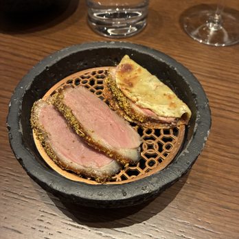 Class Act - The Duck - Seared tuna slices with a crust are presented in a black bowl on a wooden table, accompanied by a glass of water and a wine glass. - New American Near Me - Chicago, Illinois
