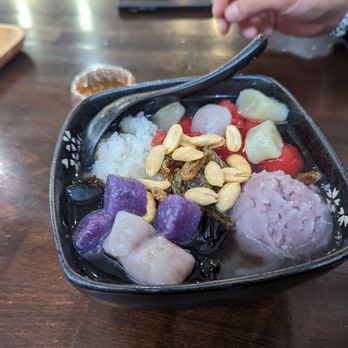 Icy Melon - A bowl of Asian dessert featuring various colorful ingredients, toppings, and a spoon, placed on a wooden table. - Desserts Near Me - Edison, New Jersey