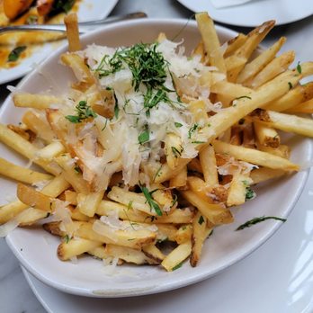 RH Chicago | The Gallery at the Three Arts Club - Truffle fries - A bowl of French fries garnished with grated cheese and chopped herbs, served on a white dish in a restaurant setting. - Furniture Stores Near Me - Chicago, Illinois