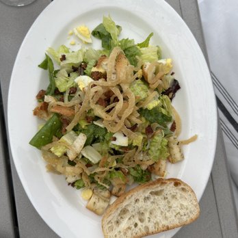 Il Mito Cafe - Insalata Cesar - A Caesar salad with lettuce, croutons, bacon bits, and shredded cheese, served with a slice of bread on a white oval plate. - Italian Near Me - Delafield, Wisconsin