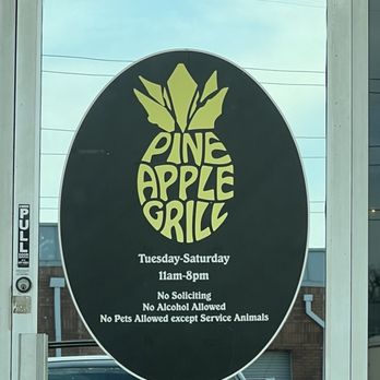 Pineapple Grill  - Hours - Door sign for Pine Apple Grill features a black background with a yellow pineapple logo at the top. The sign lists business hours as Tuesday through Saturday, 11am to 8pm. It also states policies including no soliciting, no alcohol, and no pets allowed except service animals. The sign is attached to a glass door with a push handle and is part of a storefront setting. - Hawaiian Near Me - Hurst, Texas