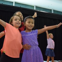 Imagination Stage - Three children pose together with arms outstretched an big smiles.  There is a child in the background who is also posing.