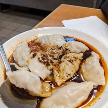 Wild Ginger - Pork Dumplings - Dumplings served in a white bowl with spicy soy sauce, chili oil, and garlic, on a wooden table at a restaurant. - Chinese Near Me - Alameda, California