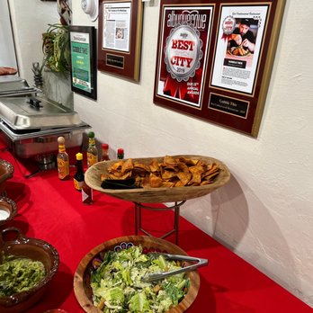 Gobble This - A buffet-style setup with chips and salad on a red table, with framed awards and articles on the wall behind, in a restaurant setting. - Salvadoran Near Me - Albuquerque, New Mexico