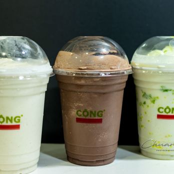Cong Caphe - Coconut Mung Bean Smoothie ($7.85), Coconut Cocoa Smoothie ($7.85), Coconut Green Rice Smoothie ($8.10) - Three smoothies in clear plastic cups with dome lids, labeled 'CONG', are displayed on a white surface against a dark background. - Coffee & Tea Near Me - Toronto, Ontario