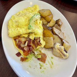 Avocadonator Omelet Avocadonator Omelet - A breakfast plate features a folded omelette with vegetables and bacon, accompanied by roasted potatoes, on a white dish.