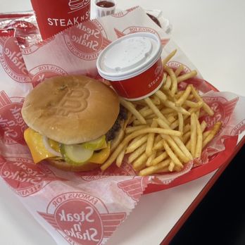 Steak ’n Shake - Bitcoin, small fry, side cheese sauce. - A meal from Steak ’n Shake includes a cheeseburger with pickles, a side of French fries, and a soft drink in a red cup. - Burgers Near Me - Glenview, Illinois