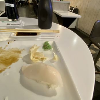 AKA Sushi - Nigiri with fruit fly at AKA. - A mostly empty sushi plate with remnants of food, wasabi, soy sauce, and chopsticks on a restaurant table, with a black soy sauce bottle and a water pitcher nearby. - Sushi Bars Near Me - Jackson, Michigan