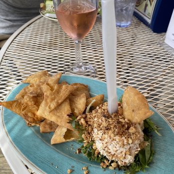 Rick's Cafe - smoked whitefish pate - Fried wontons and seafood salad with chopped nuts are served on a blue plate, accompanied by a glass of rosé wine on a metal outdoor table. - American Near Me - Leland, Michigan