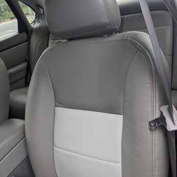Cibola Upholstery - The image shows the back of a leather car seat with a two-tone design, primarily gray with a white section in the middle. The headrest is also covered in gray leather, and the seat includes visible stitching details. The surrounding interior includes parts of the vehicle's side panel and window, with a seatbelt visible on the right side. The setting appears to be inside a vehicle, with natural light coming through the windows. - Furniture Reupholstery Near Me - Corrales, New Mexico
