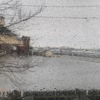 Drycrete Waterproofing - Raindrops are visible on a window screen, with a blurred view of buildings and trees outside on a rainy day. - Waterproofing Near Me - Walpole, Massachusetts