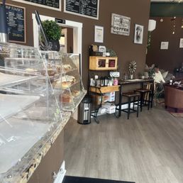 Inside - Coffee shop interior featuring menu boards, a pastry display case, and seating with a person sitting in the background.