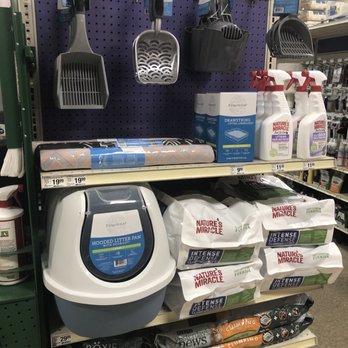 PetSmart - PetSmart aisle features cat litter in large bags, litter box accessories such as scoops and mats, and cleaning sprays. The products are arranged on shelves with visible price tags, and the background includes a purple pegboard with additional pet supplies. - Pet Stores Near Me - Oswego, Illinois