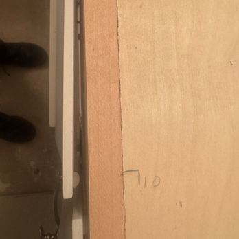 Authentic Wood Doors Carpentry - Drawer not mounted properly - A photograph captures a close-up of a wooden surface with a handwritten measurement reading '7.0' on it. The surface appears to be part of a woodworking or carpentry project. A metal tool, possibly a level or a similar instrument, is positioned on the left side of the image, partially visible. The background includes a concrete floor and a person's shoes, indicating a workshop or construction environment. - Carpenters Near Me - Santa Fe, New Mexico
